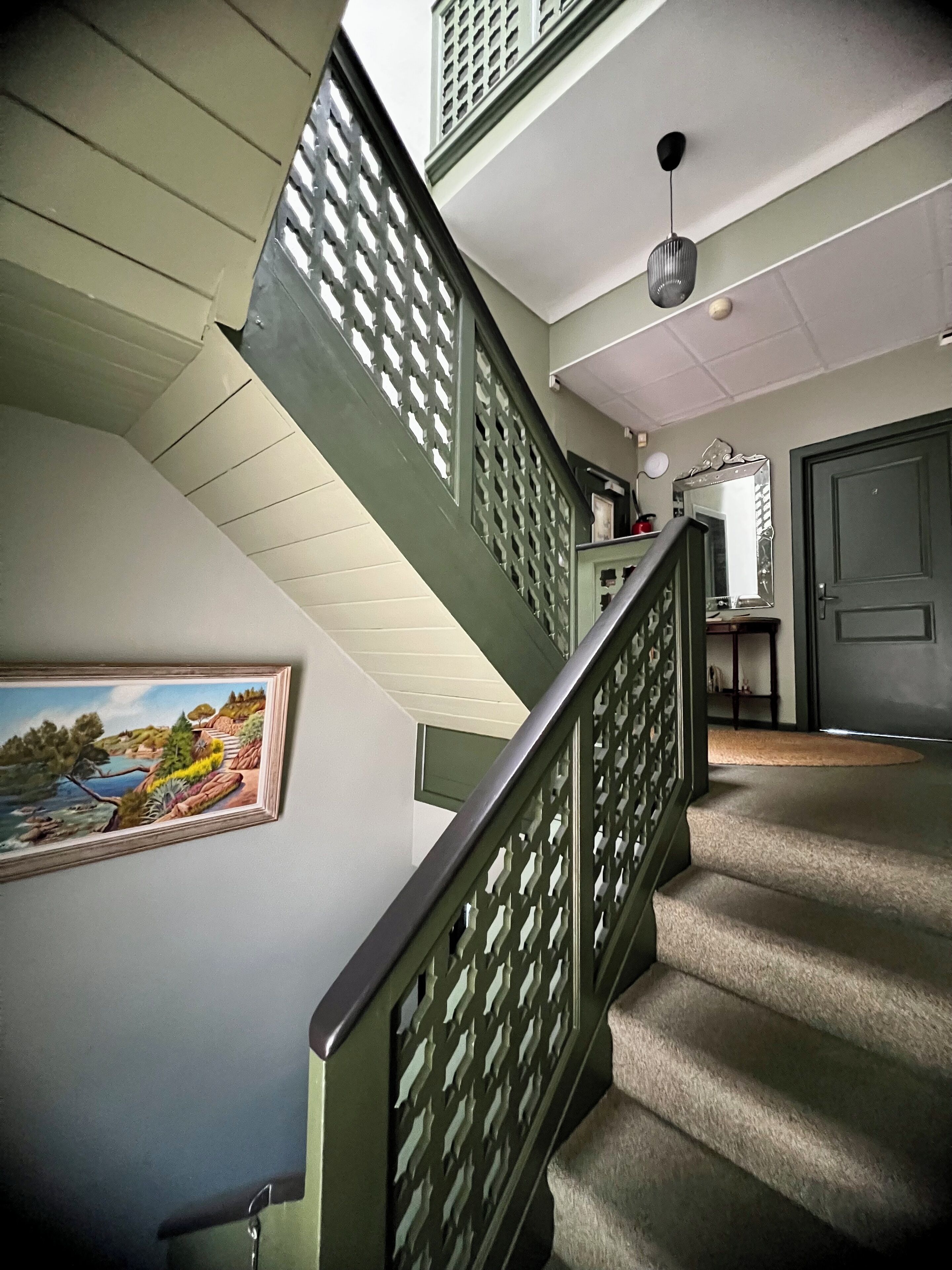Un escalier avec une rampe verte, un tableau accroché au mur et une porte au fond.