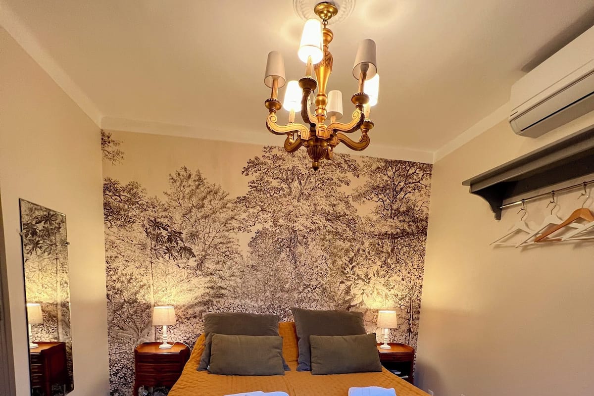 Ein Schlafzimmer mit einem großen Bett, einer Kandelaber, einer blumengemusterten Wand und einem Spiegel.