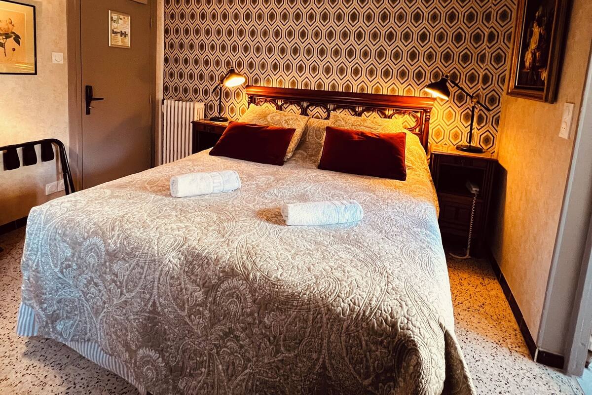 Ein Hotelzimmer mit einem großen Bett, strukturierter Tapete, einer Hängelampe, einer Tür und einem Heizkörper.