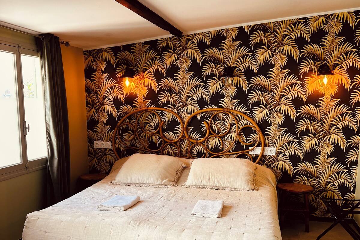 Ein Bett mit weißer Decke, ein Fenster mit Vorhängen und eine Wand mit einem Palmblattmuster.