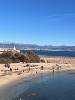 Ein Strand mit Menschen, einer Steinmauer und Bergen im Hintergrund.
