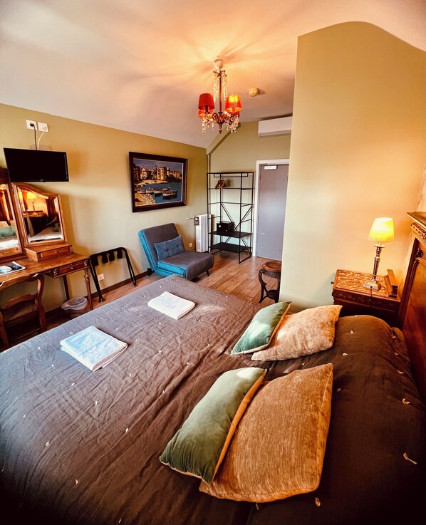 A hotel room with a bed, a desk with a mirror, a chair, a television, and a painting on the wall.
