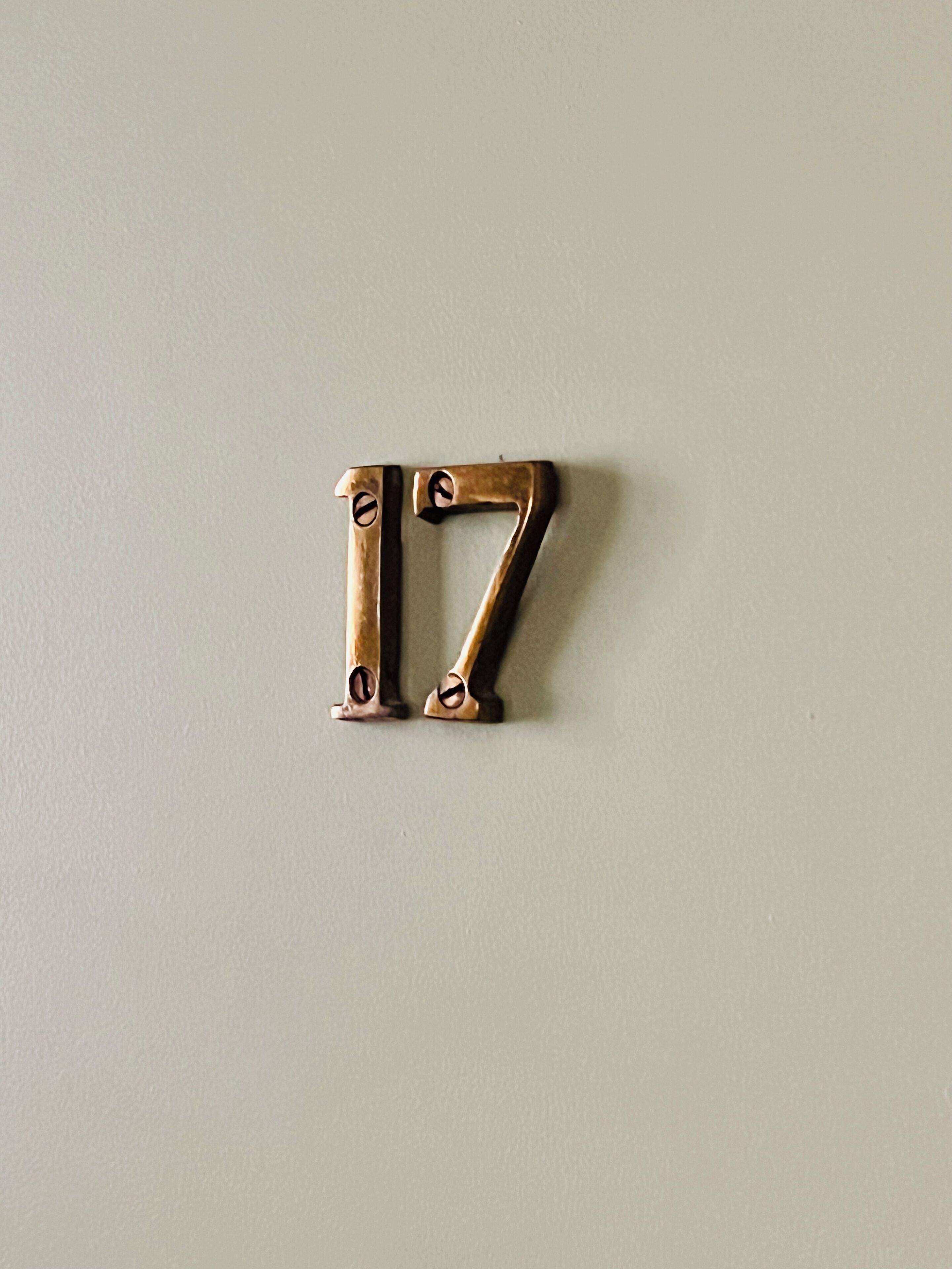 A brass number 17 on a plain wall.