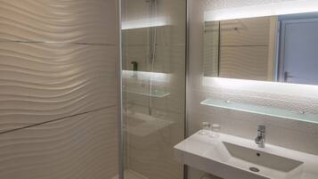 Une salle de bain moderne avec une douche à l’italienne en verre, un lavabo blanc avec un miroir au-dessus et un mur à texture.