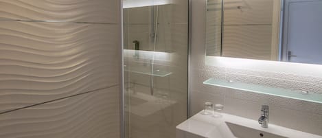 Un baño moderno con cabina de ducha de vidrio, un lavabo blanco con espejo superior y una pared con textura.