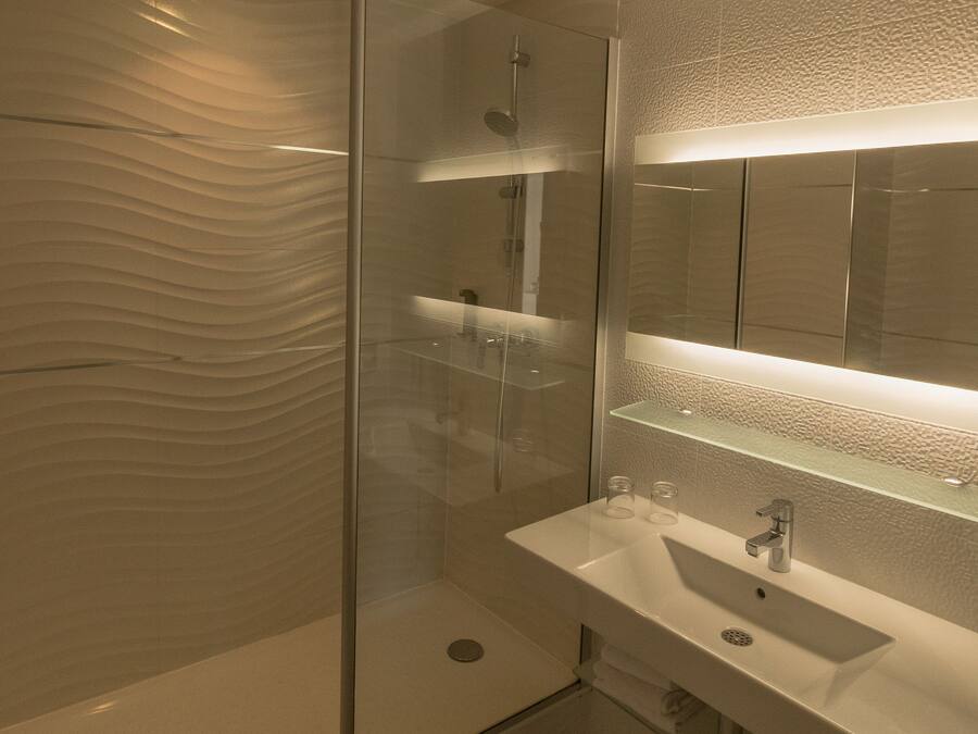 Un baño moderno con ducha de vidrio, un espejo grande y un lavamanos blanco.