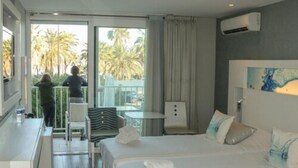 Une chambre d’hôtel comprenant un lit, un bureau, une chaise, une petite table et un balcon avec vue sur les palmiers.