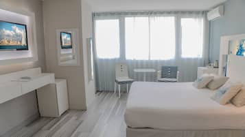 Camera d'albergo con un letto, una scrivania, una sedia, una TV e una finestra con tende.