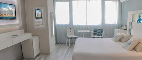 Une chambre d’hôtel avec un lit, un bureau, une chaise, une télévision et une fenêtre avec des rideaux.