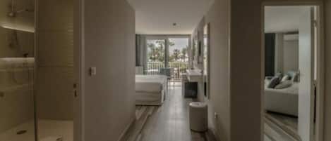 A modern hotel room with a shower, a bed, a seating area, and a balcony with a view.
