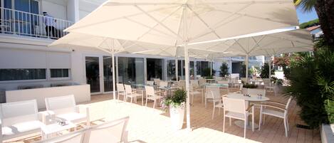 An outdoor patio area with white furniture, including tables and chairs, under large white umbrellas.