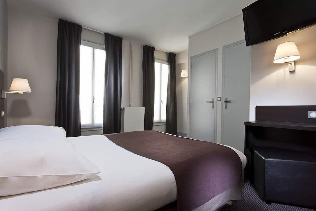 A hotel room with a bed, a desk, a TV, and a window with curtains.
