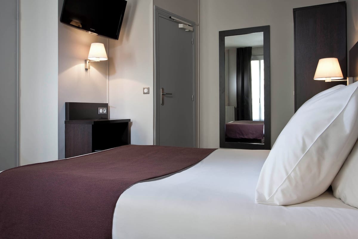 A hotel room with a bed, a TV mounted on the wall, a bedside table, and a mirror.