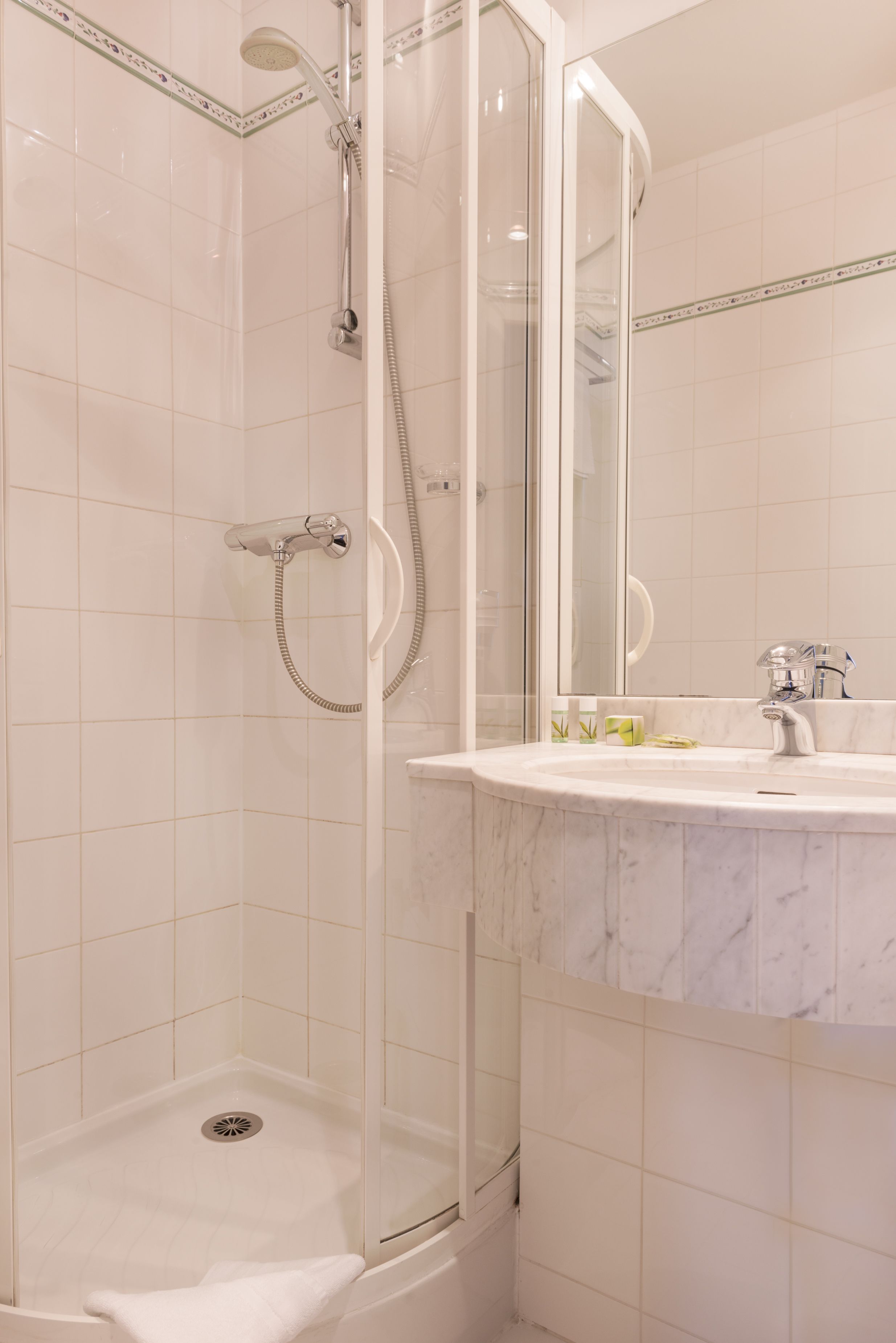 A modern bathroom with a glass-enclosed shower, a marble sink, and a large mirror.