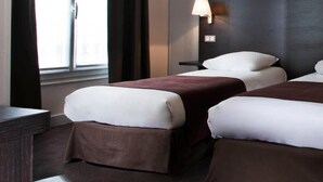 A hotel room with two beds, a nightstand, a lamp, and a window with curtains. - Hôtel des Ecrivains (Paris)