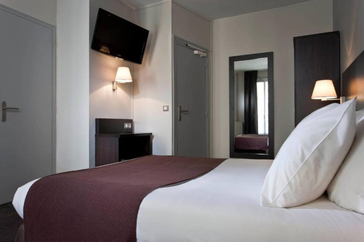 A hotel room with a large bed, a flat-screen TV mounted on the wall, a bedside table, and a mirror.