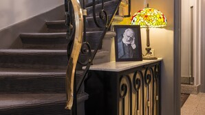 A staircase with ornate black metal railings and a decorative lamp on a console table. - Hôtel des Ecrivains (Paris)