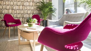 A modern interior with a round table, two vibrant chairs, and a bookshelf in the background. - Hôtel des Ecrivains (Paris)