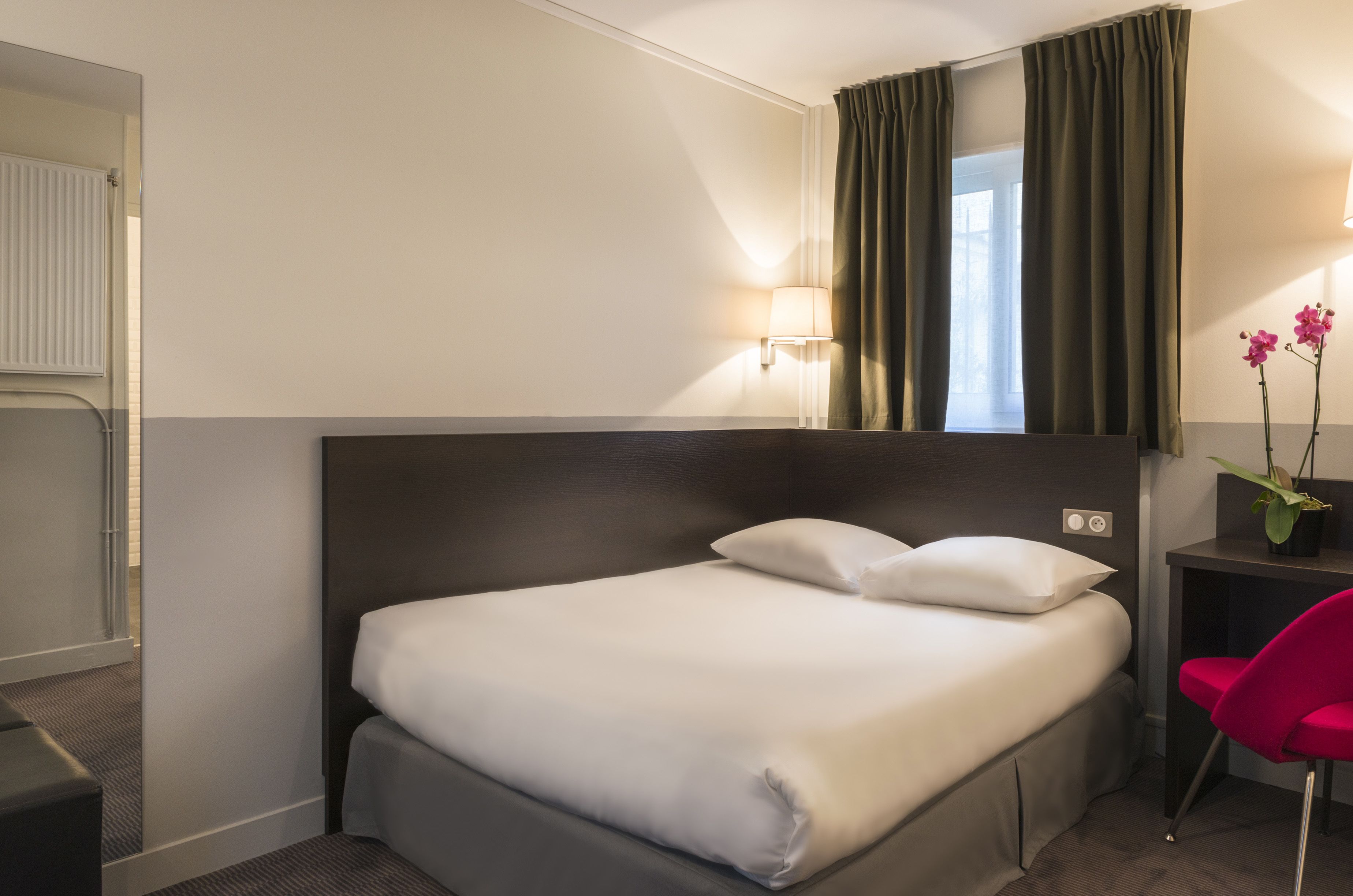 Una camera d'albergo con un letto, una scrivania con una sedia, una lampada e una pianta in vaso.