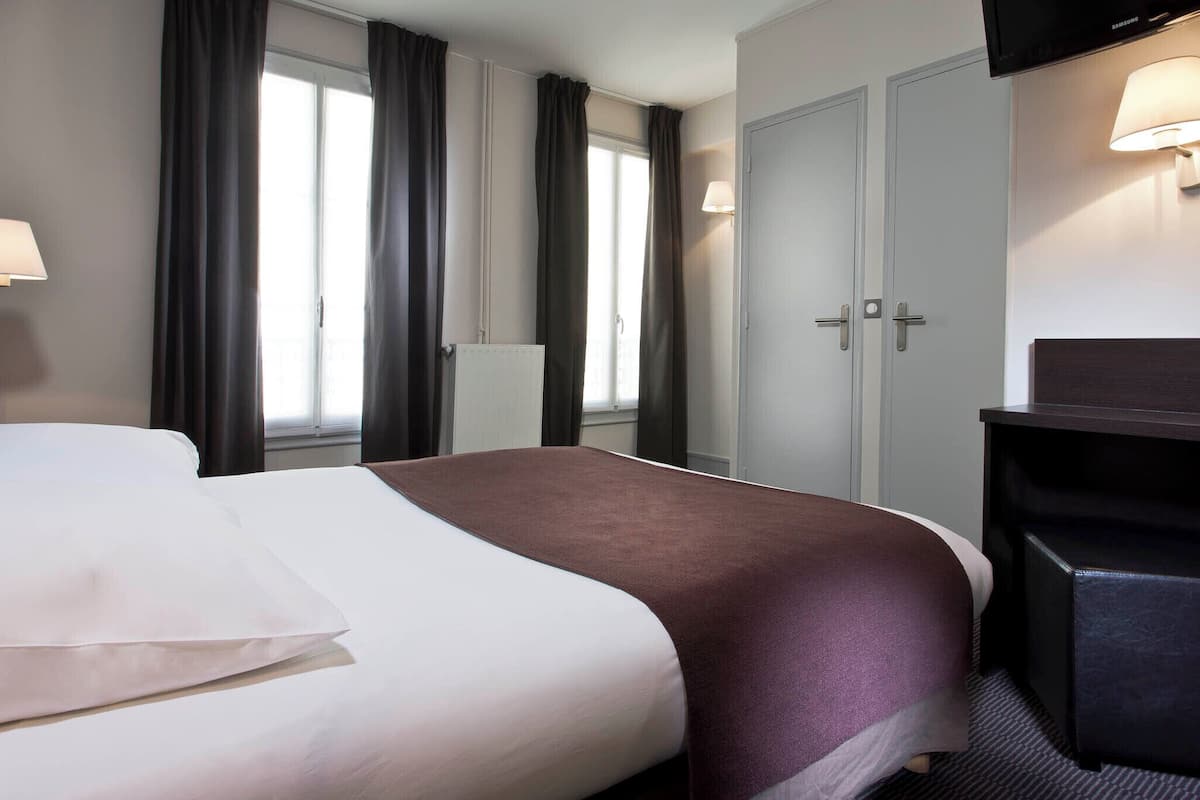 A hotel room with a bed, a desk, a chair, a wardrobe, and a lamp.