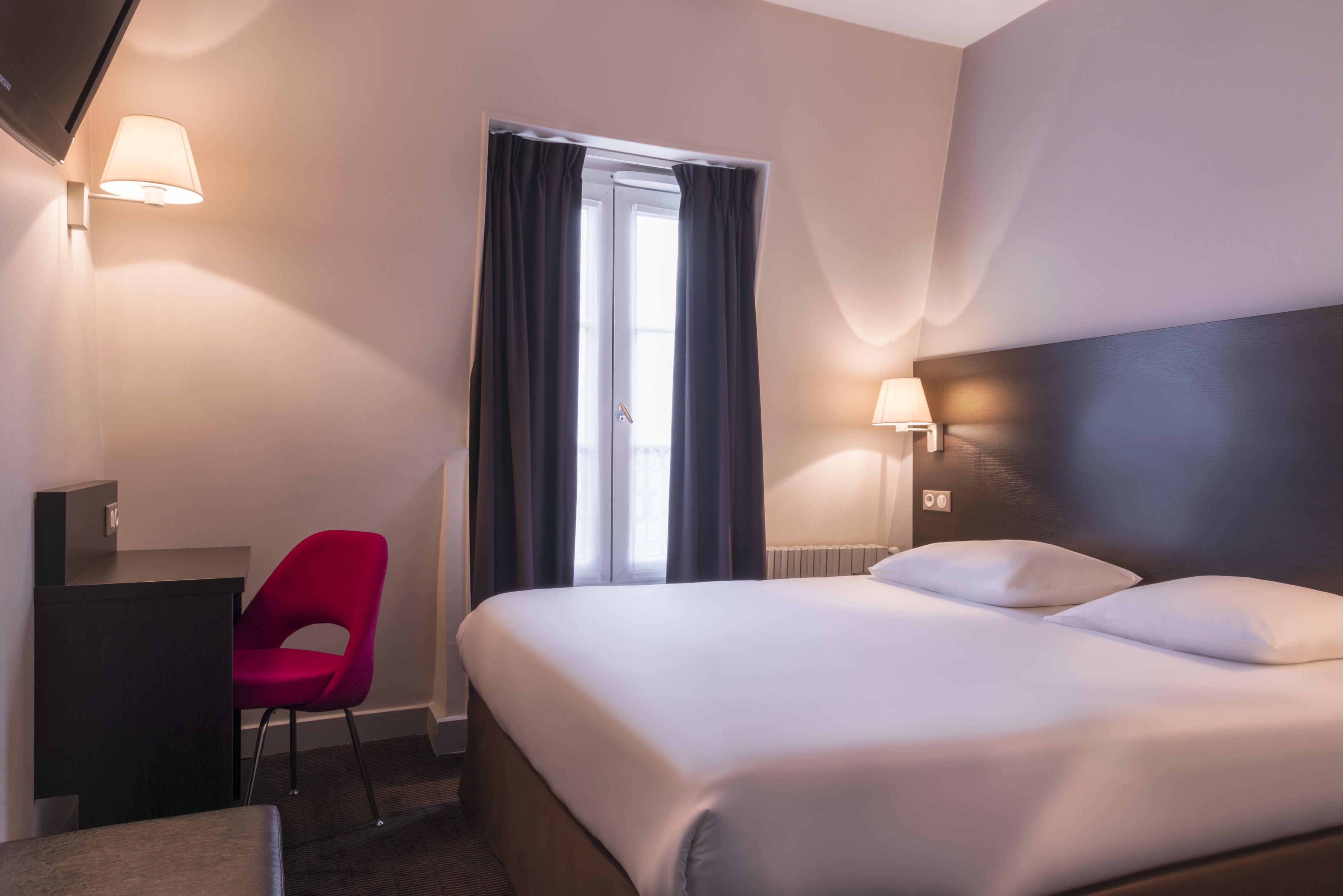 A hotel room with a bed, a desk, a chair, and two lamps.