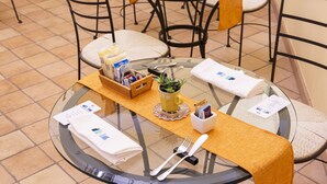 A round glass table with a yellow table runner, a small potted plant, a wooden box with magazines, and neatly folded white napkins. - Quartuccio - Albergo Diffuso (Gaeta)