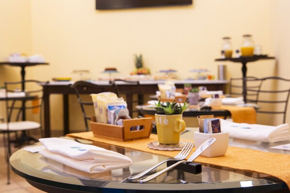 Una escena de desayuno con una mesa de vidrio, una taza amarilla, una pequeña planta y cubiertos ordenados.