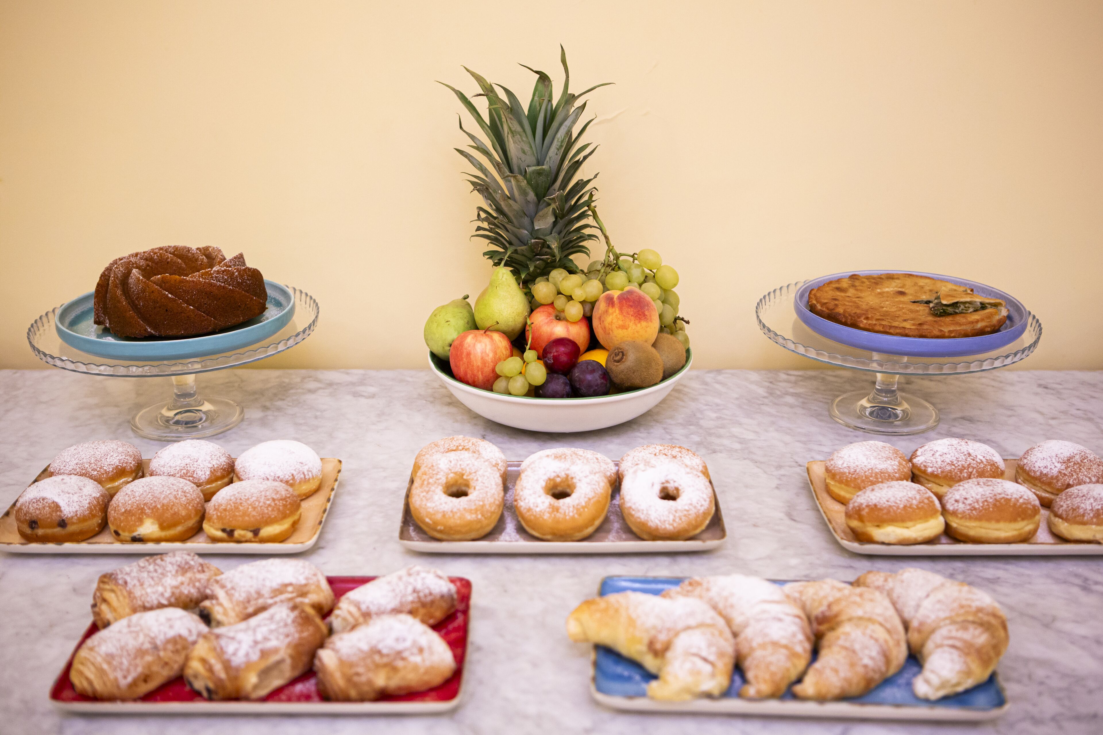Diversos postres y frutas sobre una mesa de mármol frente a una pared lisa.
