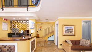 A reception area with a counter, a guitar, a staircase, and a sofa with patterned cushions. - Quartuccio - Albergo Diffuso (Gaeta)
