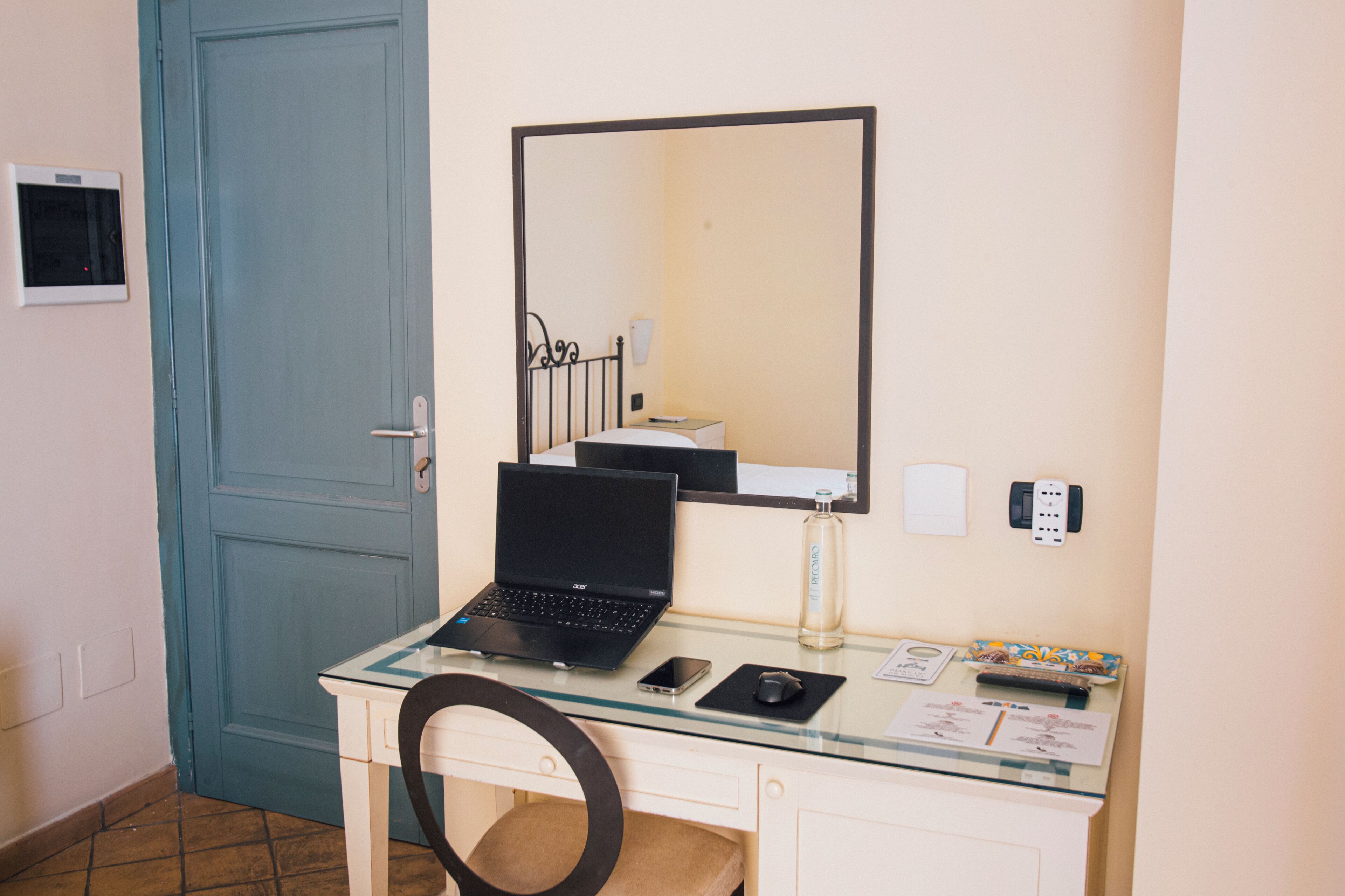 A small, tidy room with a desk, laptop, and a mirror.