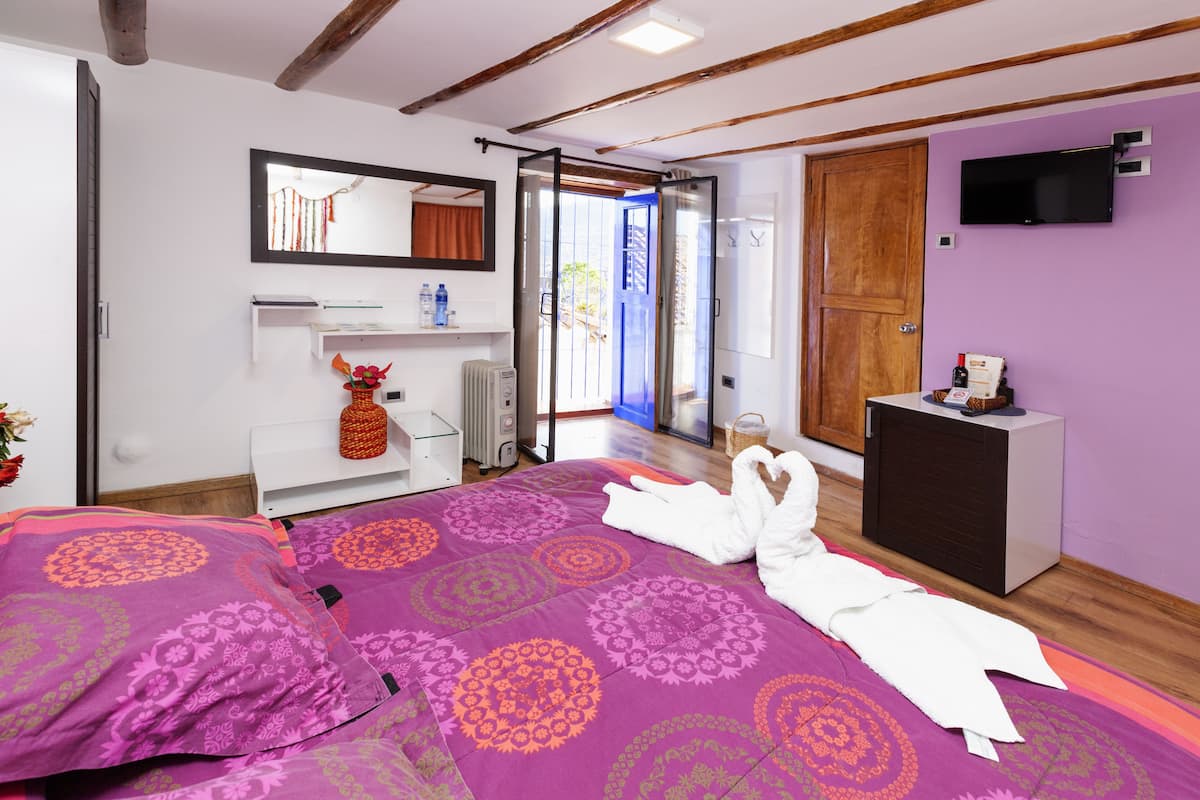 Un dormitorio con cama, una mesita de noche, televisor, armario y baño visible a través de una puerta abierta.