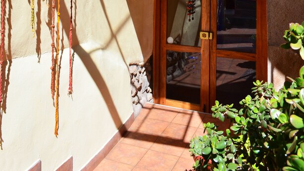 A balcony with a wooden railing, a potted plant, and a door with glass panels. - Casona les Pleiades (Cusco)