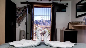 A hotel room with a bed, a window with a view of mountains, a heater, and a small cabinet. - Casona les Pleiades (Cusco)