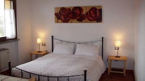 Une chambre à coucher avec un lit, deux tables de chevet, une fenêtre avec des rideaux et un tableau représentant des roses accroché au mur.