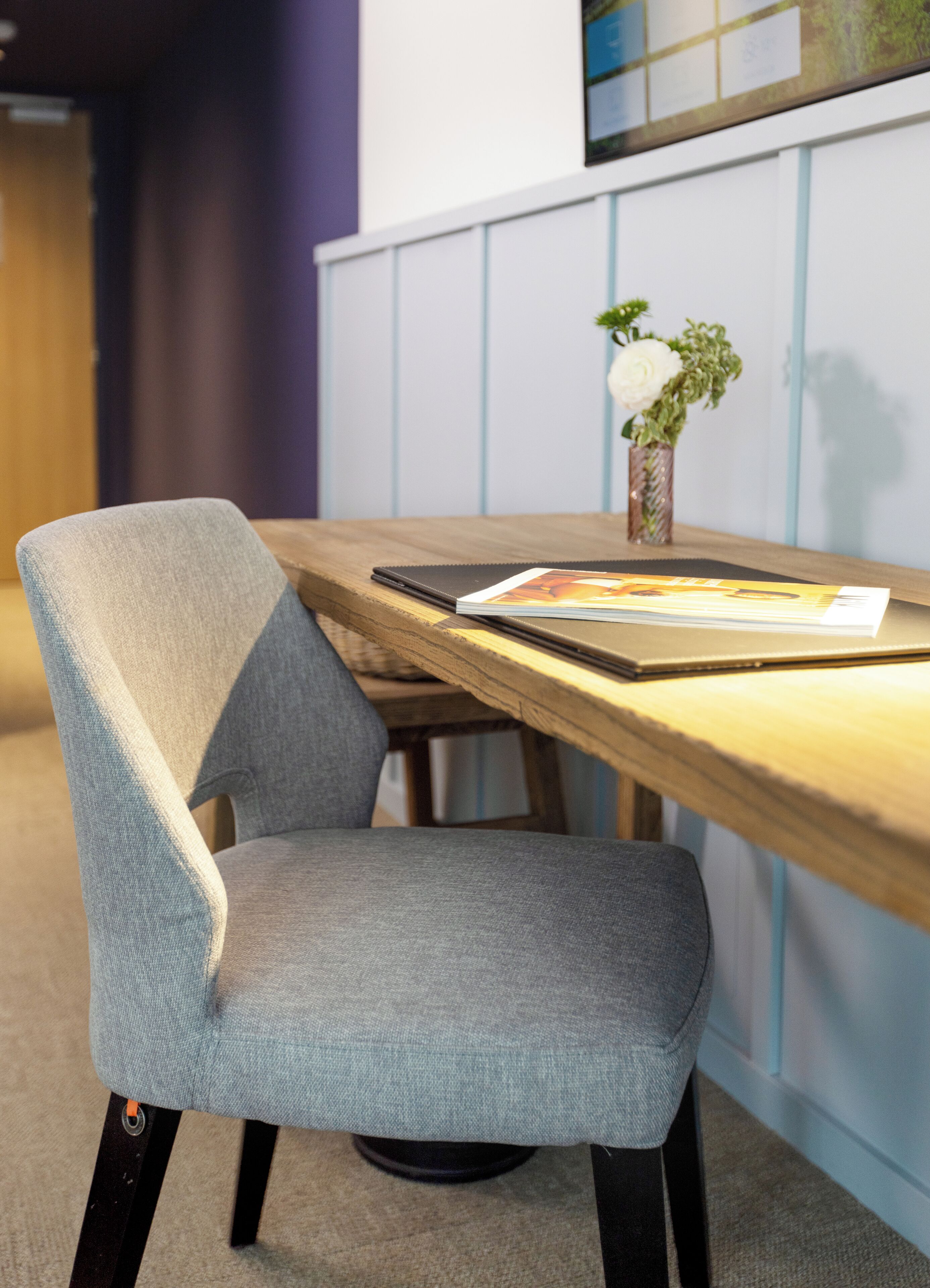 A modern office chair with a grey fabric seat and backrest, positioned at a wooden table with a magazine and a small potted plant.