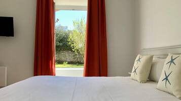 A hotel room with a large bed, red curtains, and a view of greenery outside.