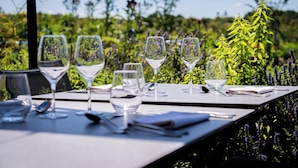 Un tavolo apparecchiato all'aperto con bicchieri da vino, bicchieri d'acqua e posateria, immerso nel verde.