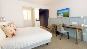 Habitación de hotel con cama, escritorio y silla. Hay un televisor en la pared y una ventana con vistas al exterior.