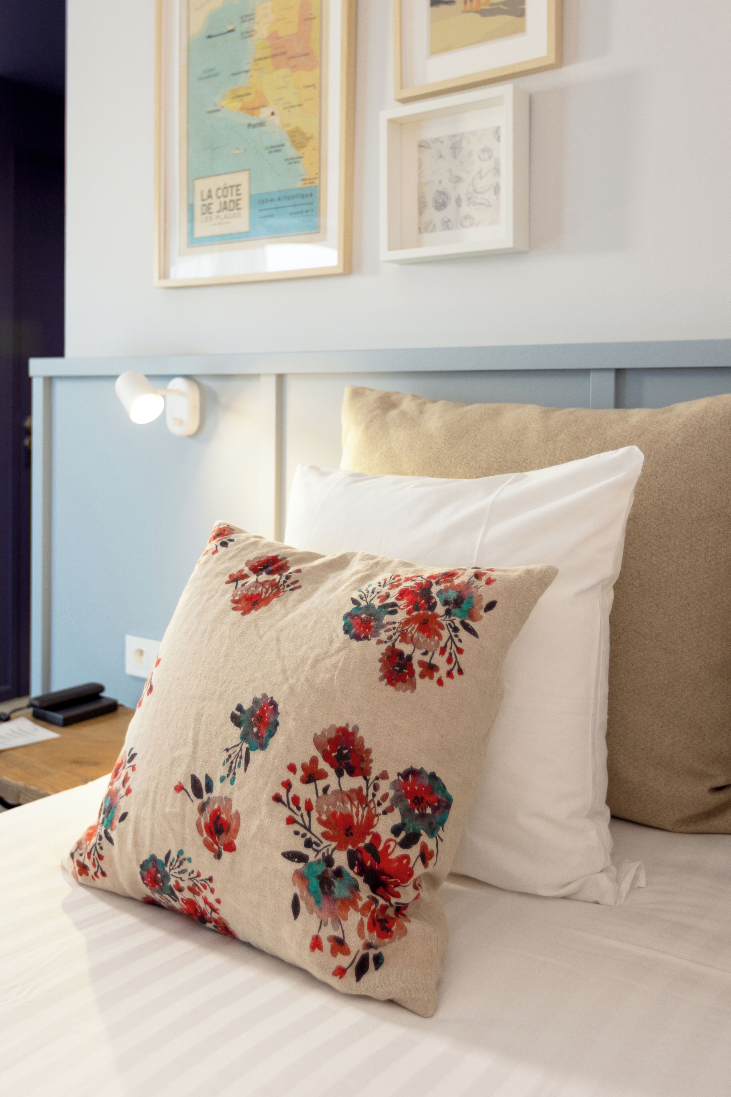A bed with floral pillows, a map on the wall, and a bedside lamp.