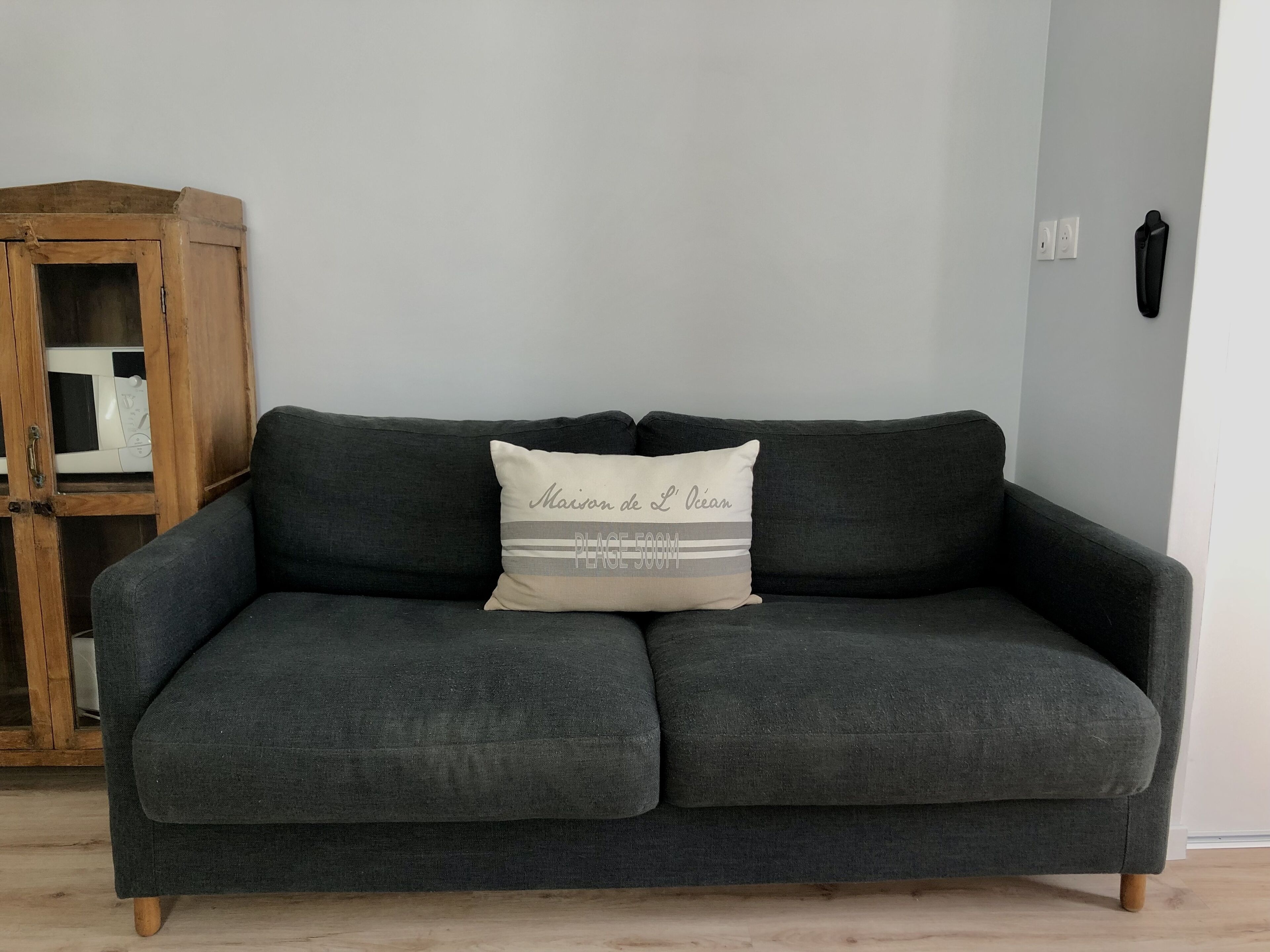 A dark grey sofa with a cushion that reads "Maison de L'Océan PLAGE 500m".