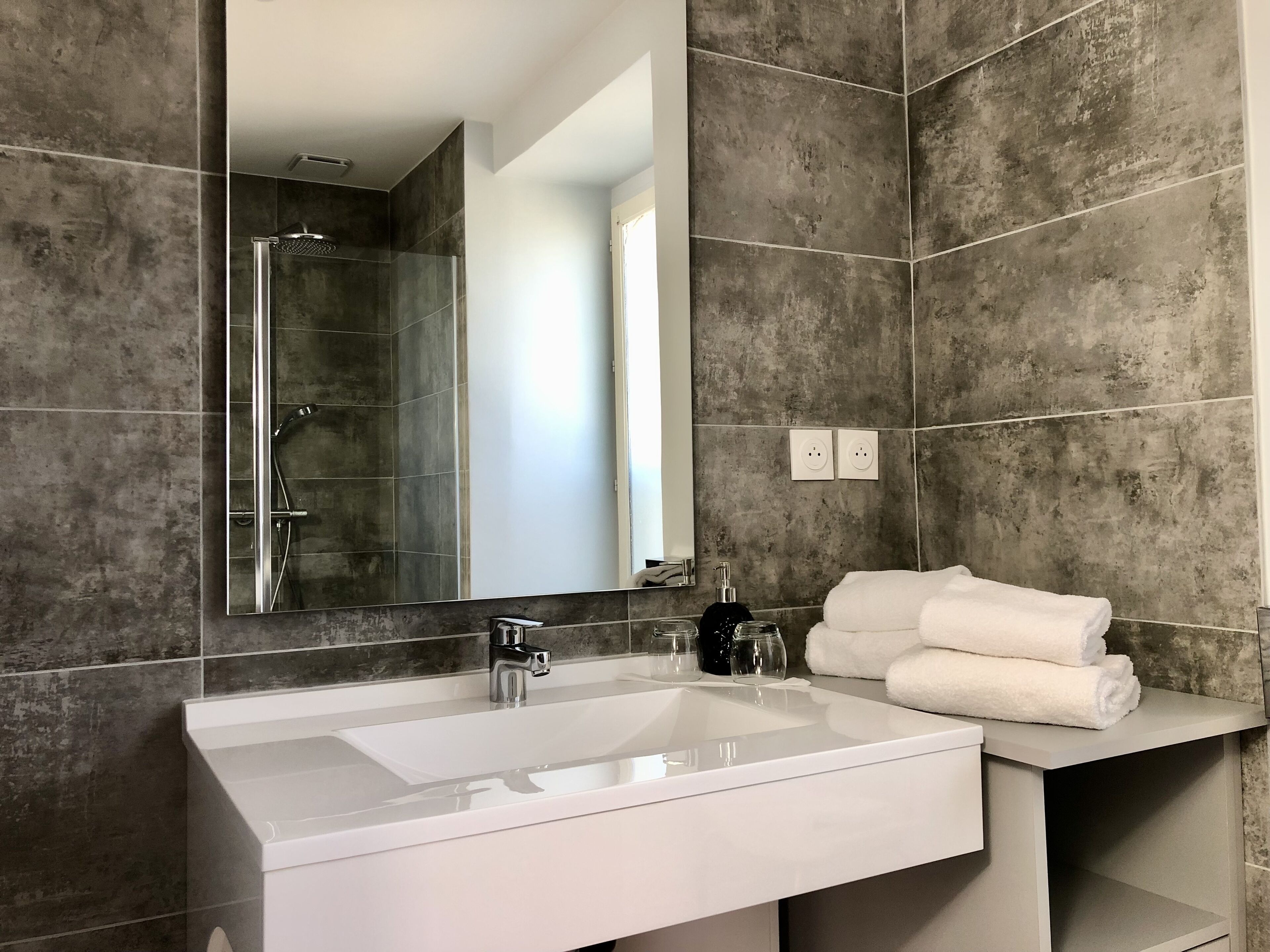 A modern bathroom with a large mirror, a white sink, and a shower area.
