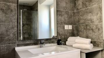 A modern bathroom with a large mirror, a white sink, and a shower area.