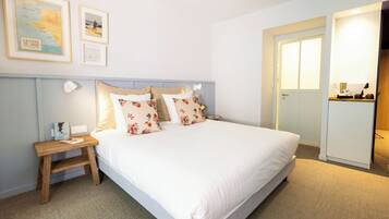 A neatly made bed with floral pillows, a small wooden nightstand with a lamp, and a framed map on the wall.
