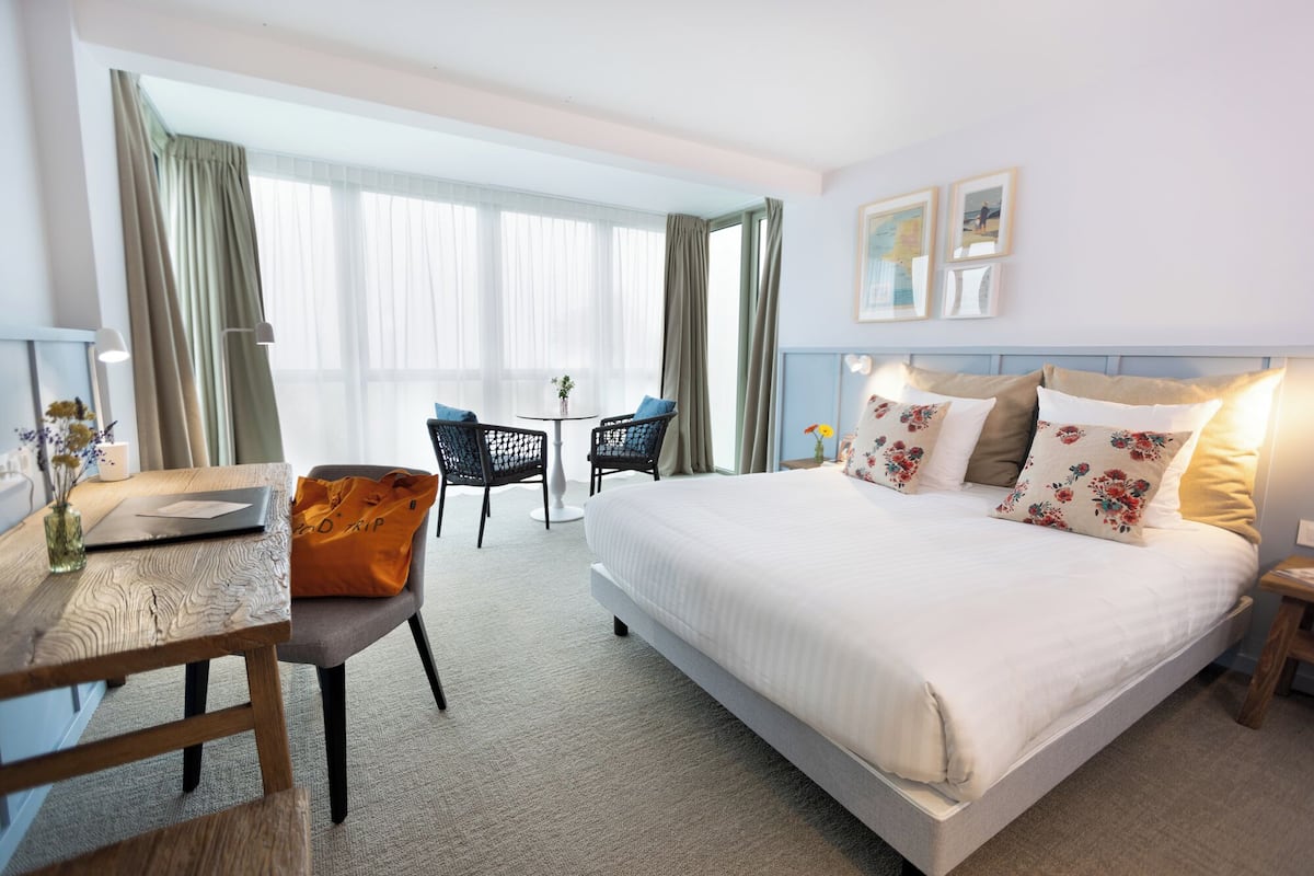 A hotel room with a bed, a desk, a chair, and a small table.