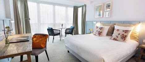 A hotel room with a bed, a desk, a chair, and a small table.