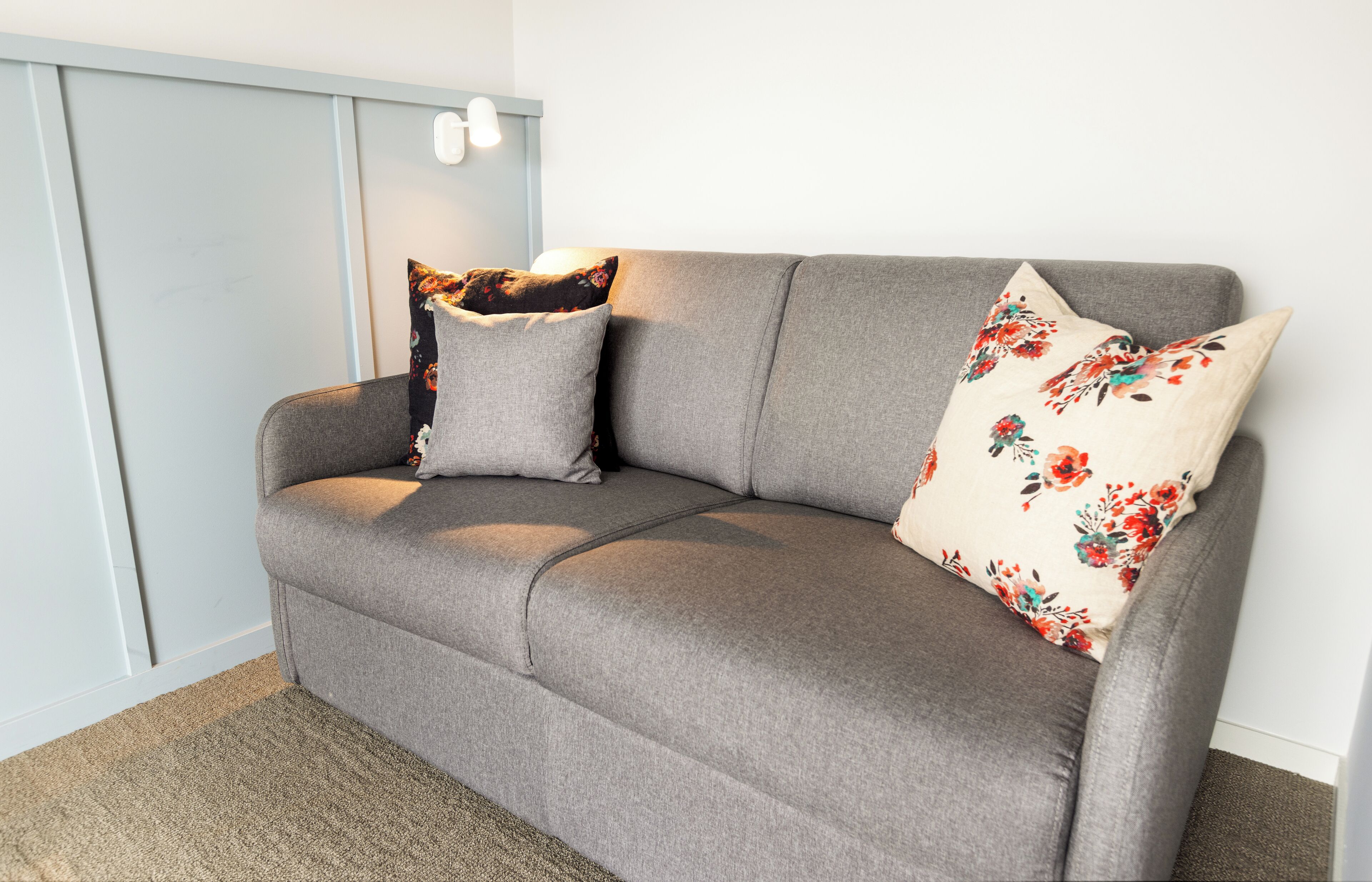 A grey sofa with floral cushions and a light-colored rug.