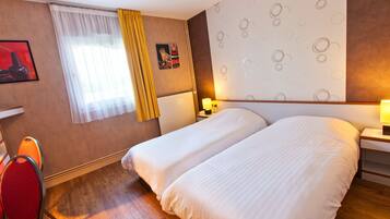 Habitación de hotel con dos camas, una silla roja, un ventanal con cortinas amarillas, un radiador y una pared con un diseño circular.