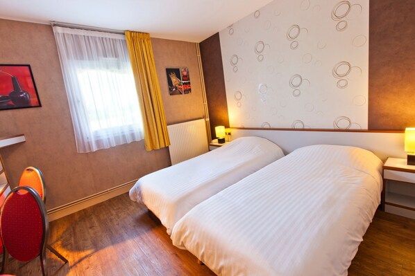 A hotel room with two beds, a red chair, a window with yellow curtains, a radiator, and a wall with a circular pattern. - Citotel Du Circuit (Magny-Cours)