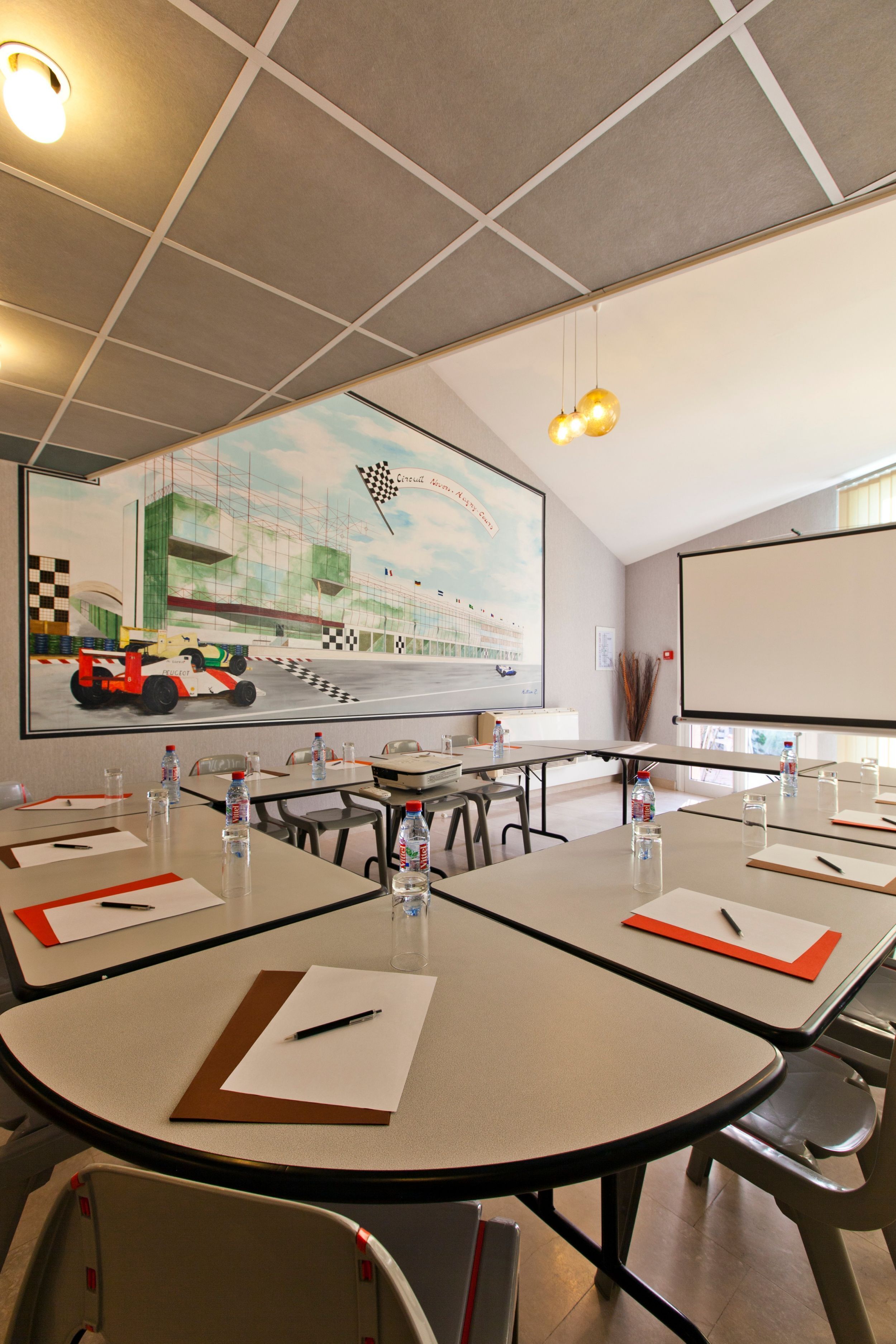 A conference room with round tables, chairs, and a large screen displaying a racing track.