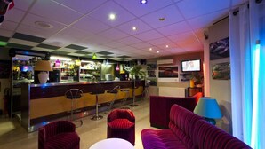 Un hall de hotel con zona de bar, asientos y una pantalla de televisión.